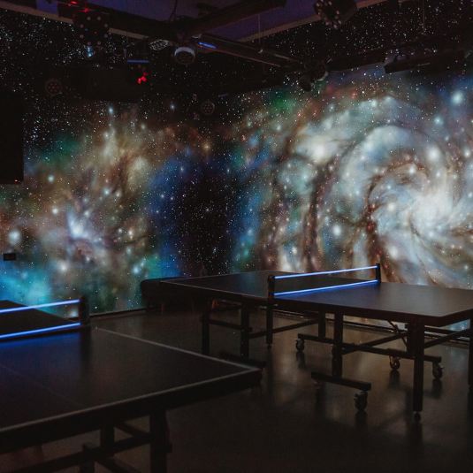The Galaxy Room at ClinkNOORD hostel in Amsterdam with a solar system mural on the walls and table tennis tables