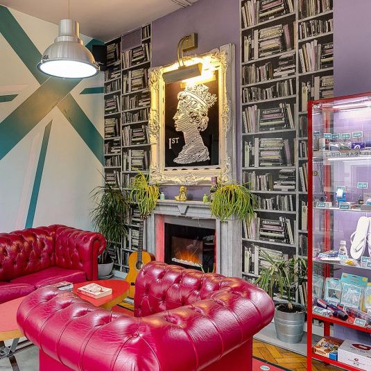 Uno spazio sociale nell'ostello Clink 261 di Londra con un divano rosso, opere d'arte e un negozio di viaggi.