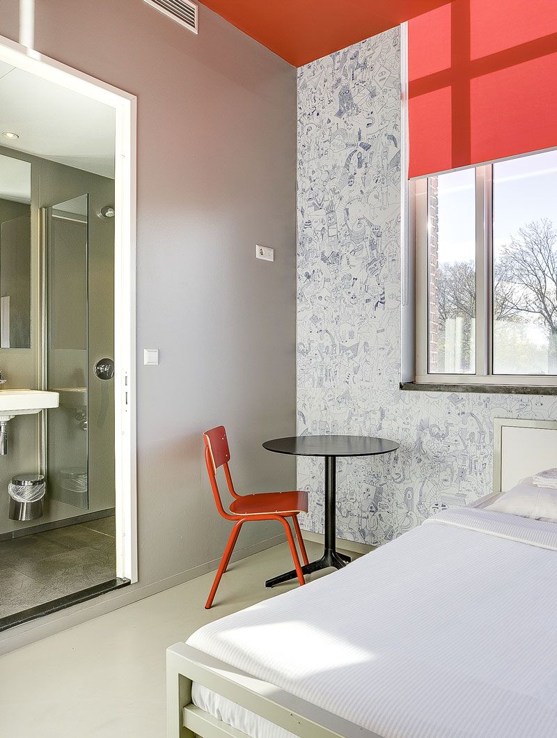 Una camera privata al ClinkNOORD Hostel di Amsterdam con letto matrimoniale, sedia, tavolo, bagno privato, carta da parati decorata e finestra.