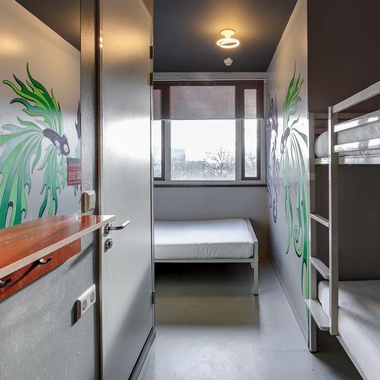 A family room at ClinkNOORD hostel in Amsterdam with a double bed and a set of bunk beds, along with an artistic mural on the wall