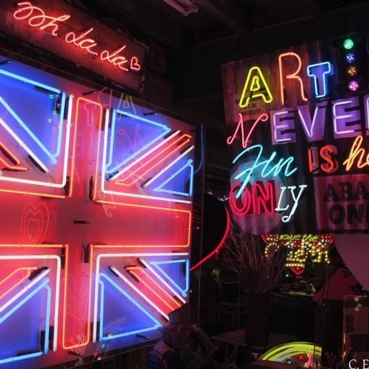 Neon lighting in London stating Art Is Never Finished, adjacent to a neon lit UK flag.