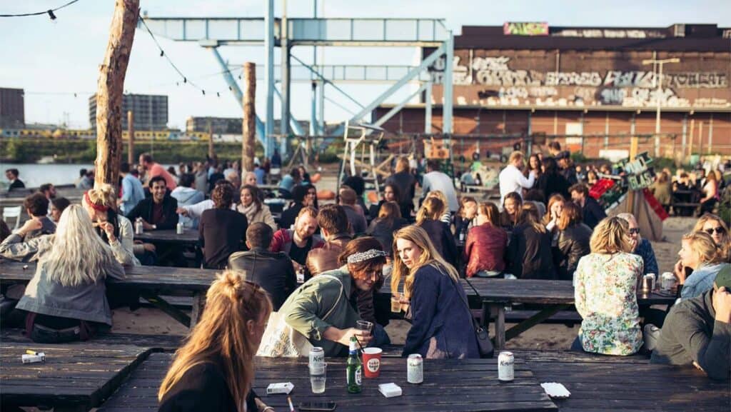 Groups of people relaxing and drinking sat on benches at Amsterdam Roest