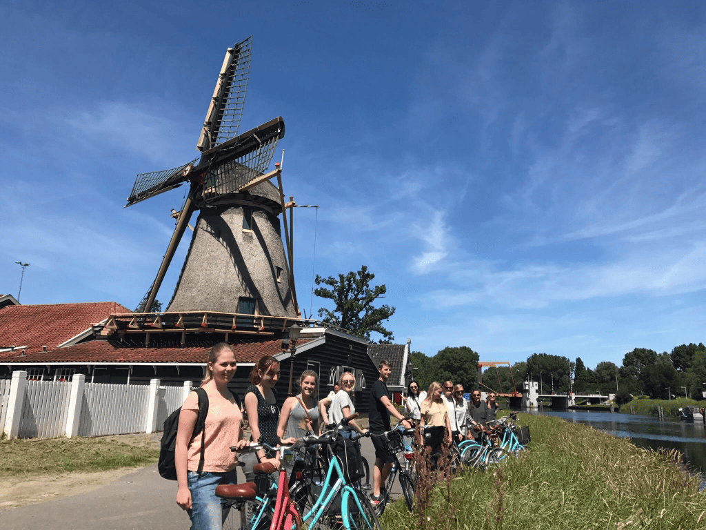 a bike tour in amsterdam with a group standing by a traditional dutch windmill
